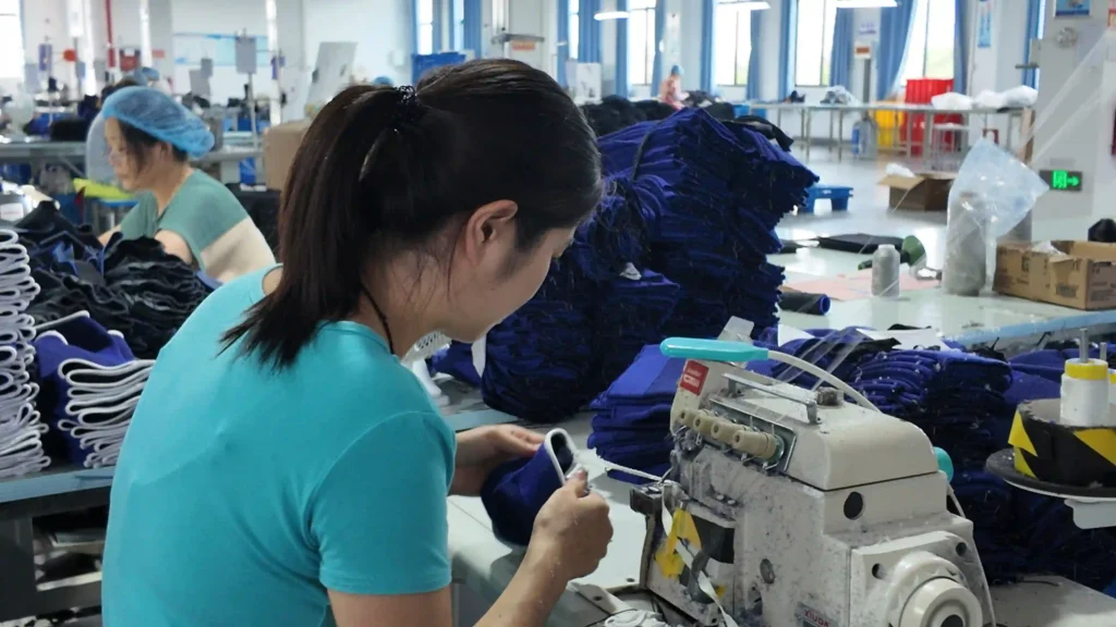 Worker sewing blue sports support components in a brace manufacturing workshop.